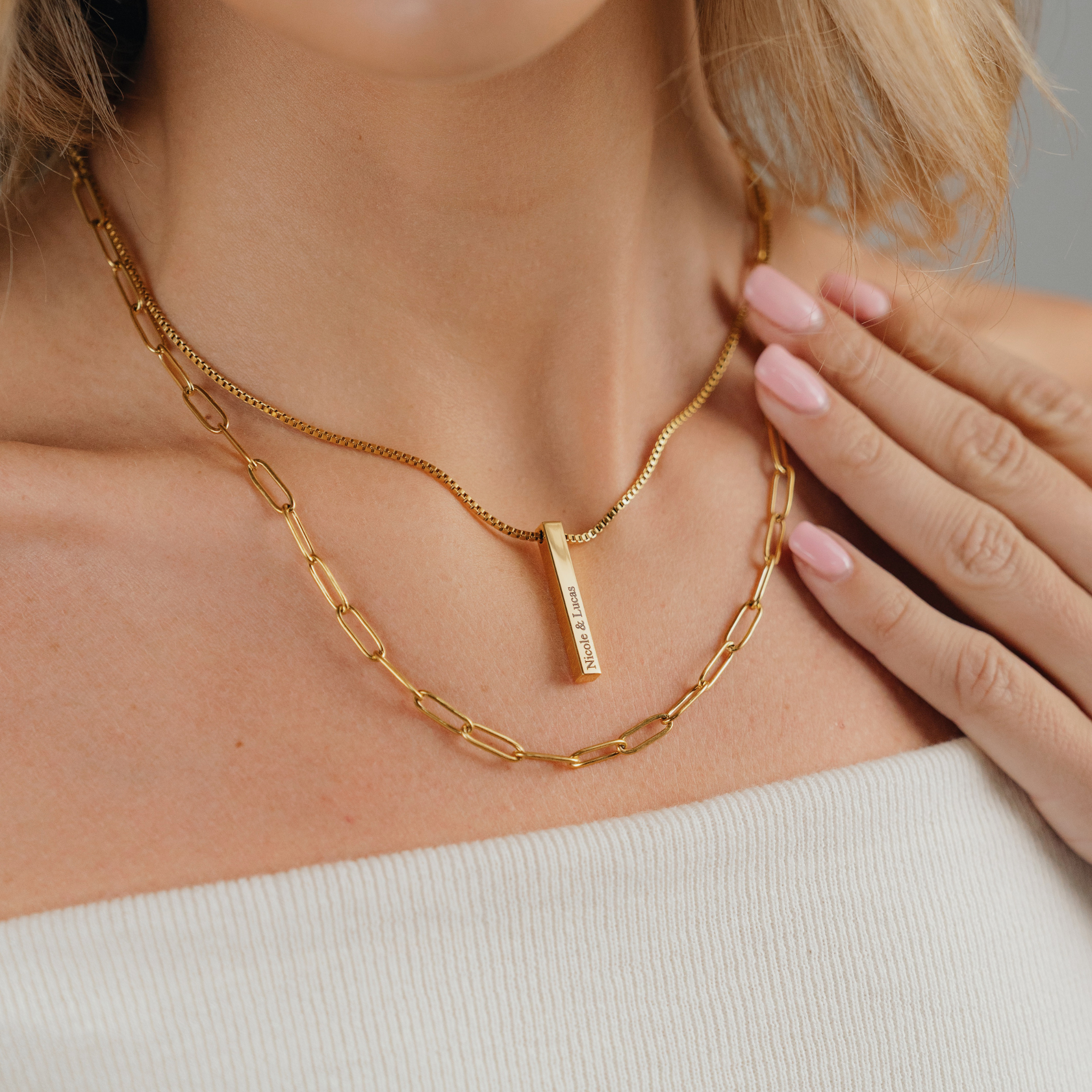 A female wearing SAAR CO's LAUREN, an 18k gold-plated Stainless Steel box pendant chain. The pendant has been engraved with Nicole & Lucas. The female is also wearing SAAR CO's 18k Gold-plated ABBIE chain.