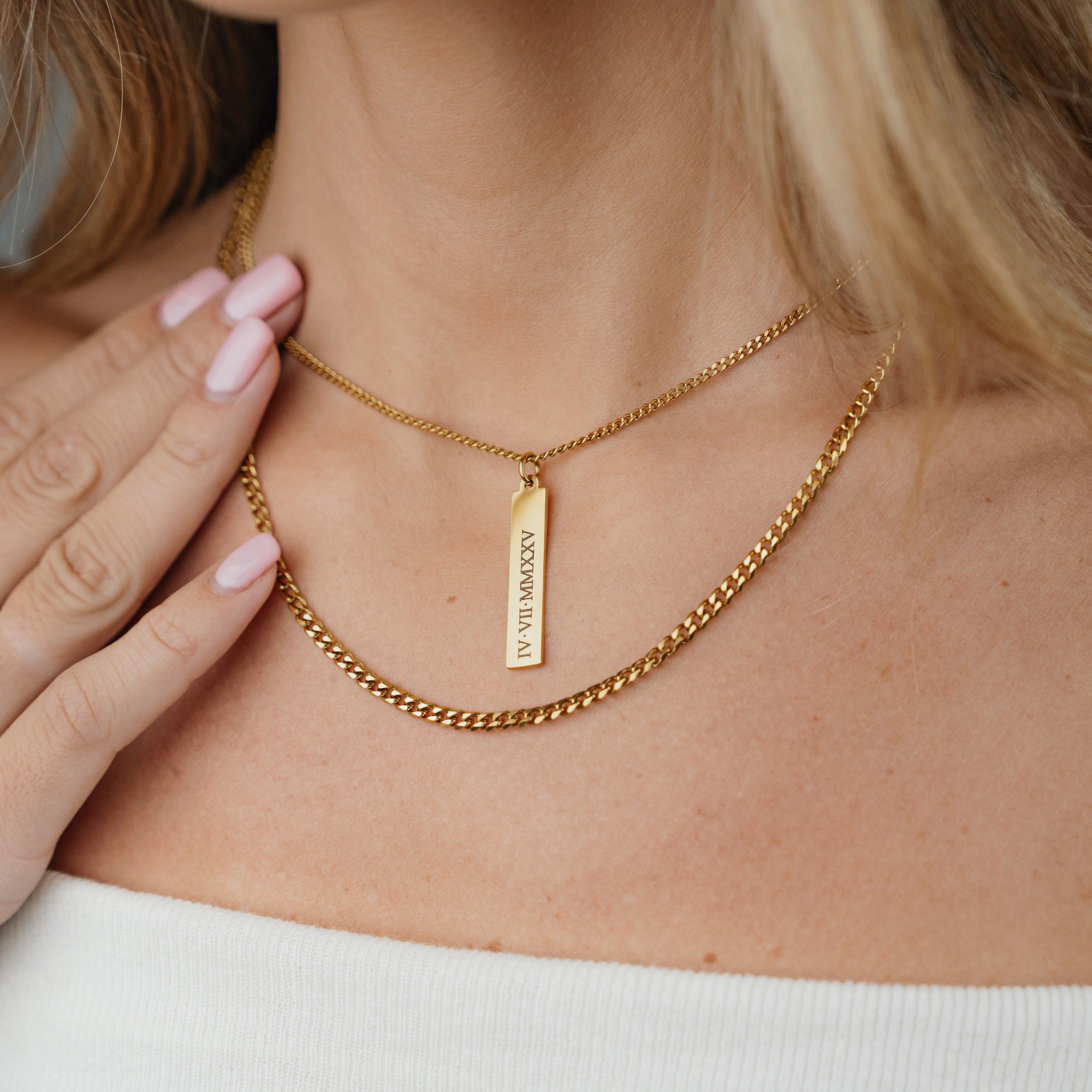 A Female wearing SAAR CO's MEGAN, a polished, 18K Gold plated pendant tag and chain. The tag has been engraved with IV.VII.MMXXV. The Female is also wearing SAAR CO's SIOBHAN, and 18K Gold 3mm Cuban chain.