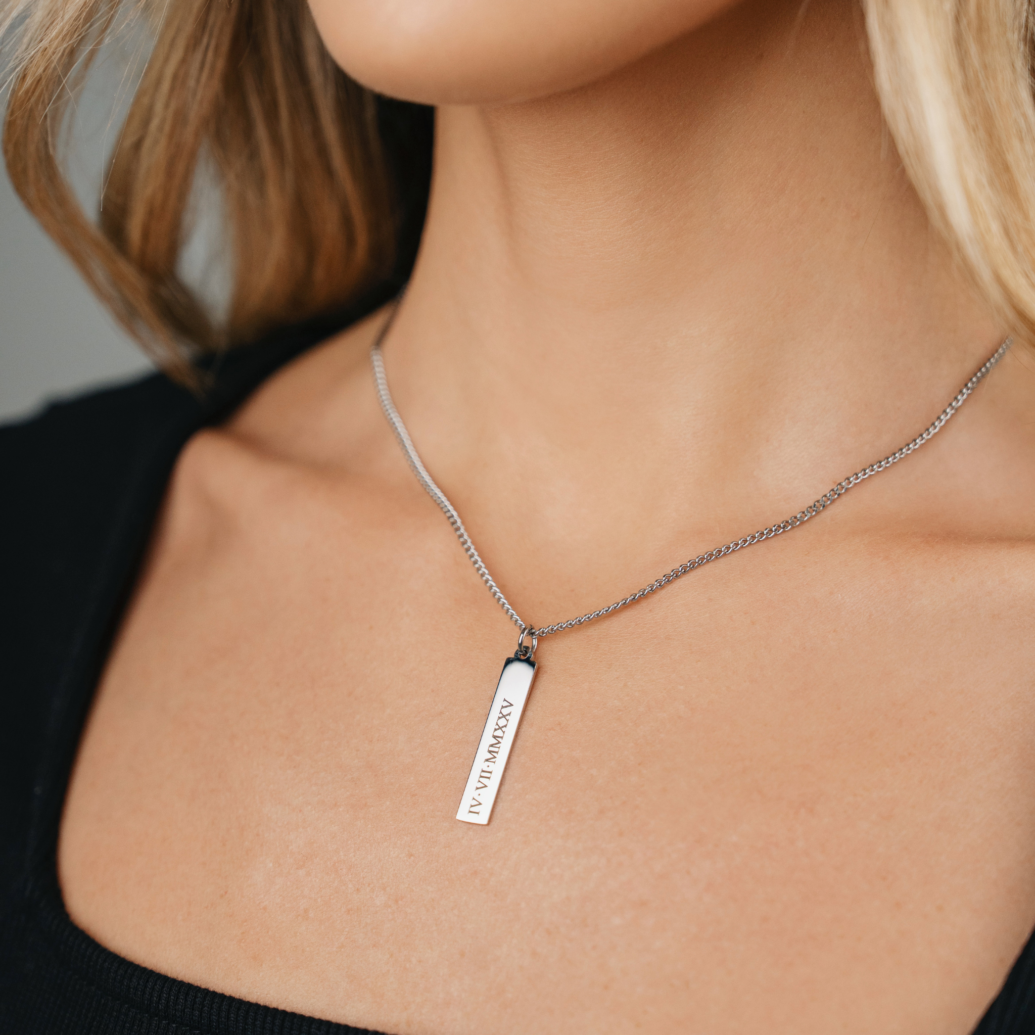 A Female wearing SAAR CO's MEGAN, a polished, stainless steel pendant tag and chain. The tag has been engraved with IV.VII.MMXXV