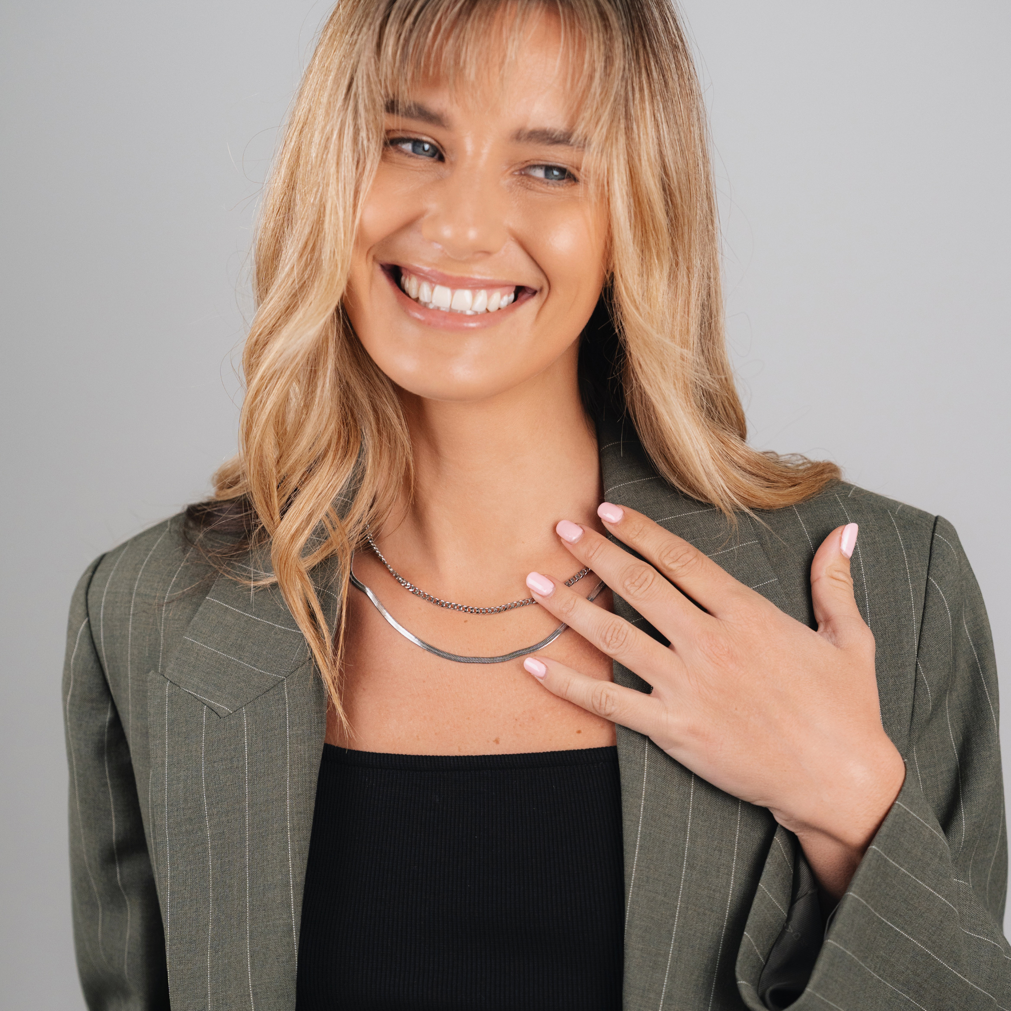 A female wearing SAAR CO's Ale, a polished, stainless steel, Snake Skin Chain. She is also wearing SAAR CO's polished, stainless steel, Madeline, a 3mm Figaro chain. 