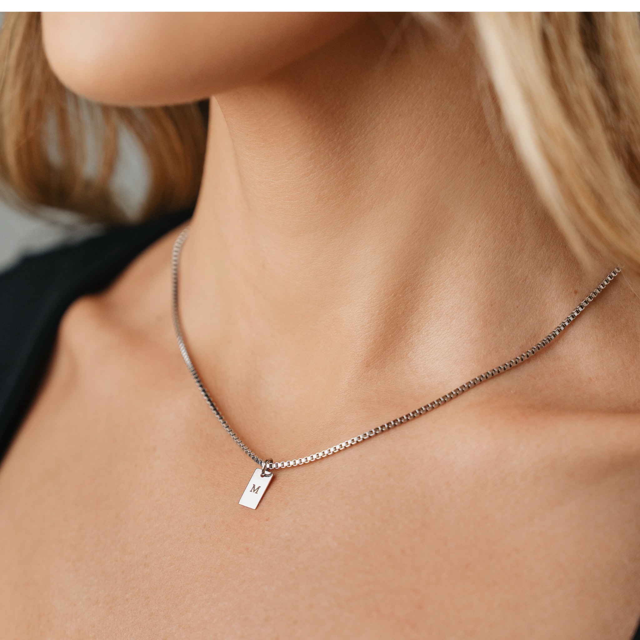 A female wearing SAAR Co's Emily, a stainless, box chain with polished pendant. The pendant has been engraved with the letter M. 