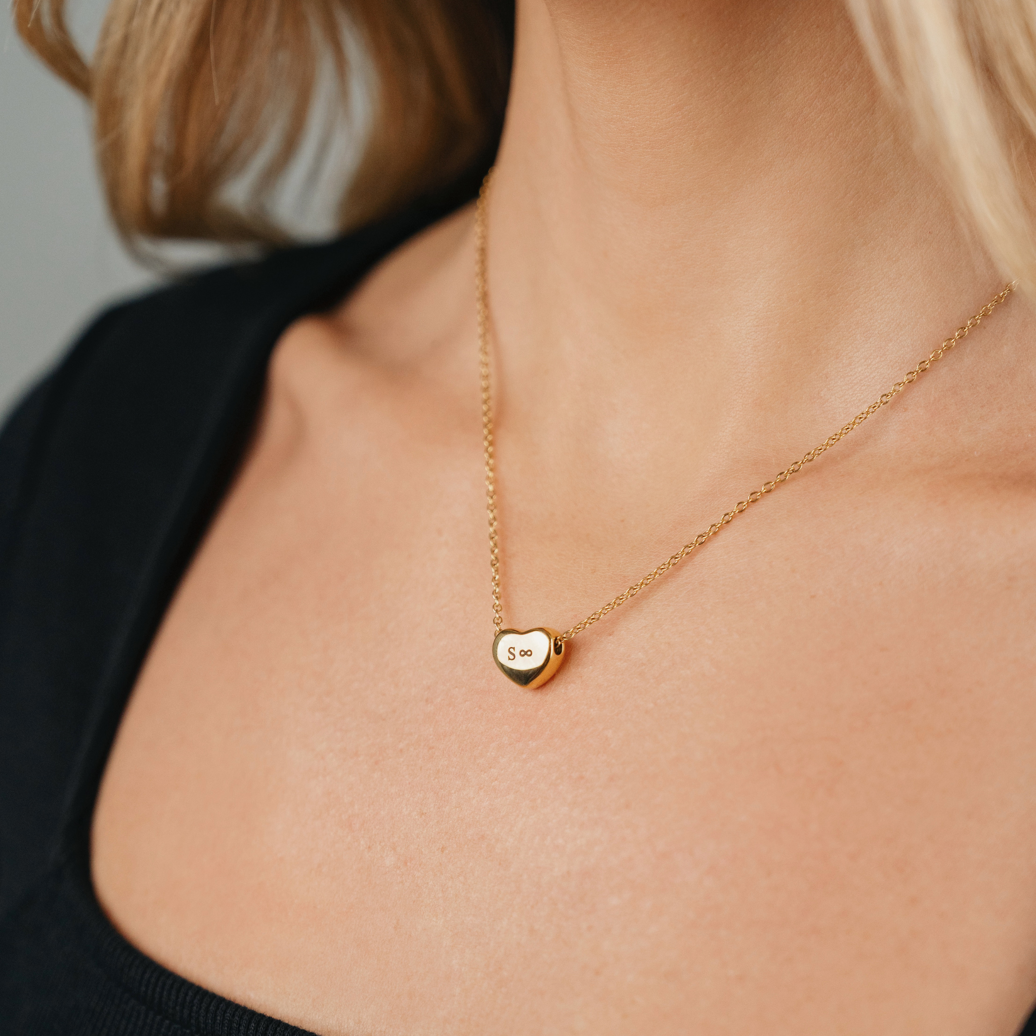 A female wearing SAAR CO's stainless steel 18k Gold coated heart pendant chain. The heart pendant is engraved with the letter S and the infinity symbol. 