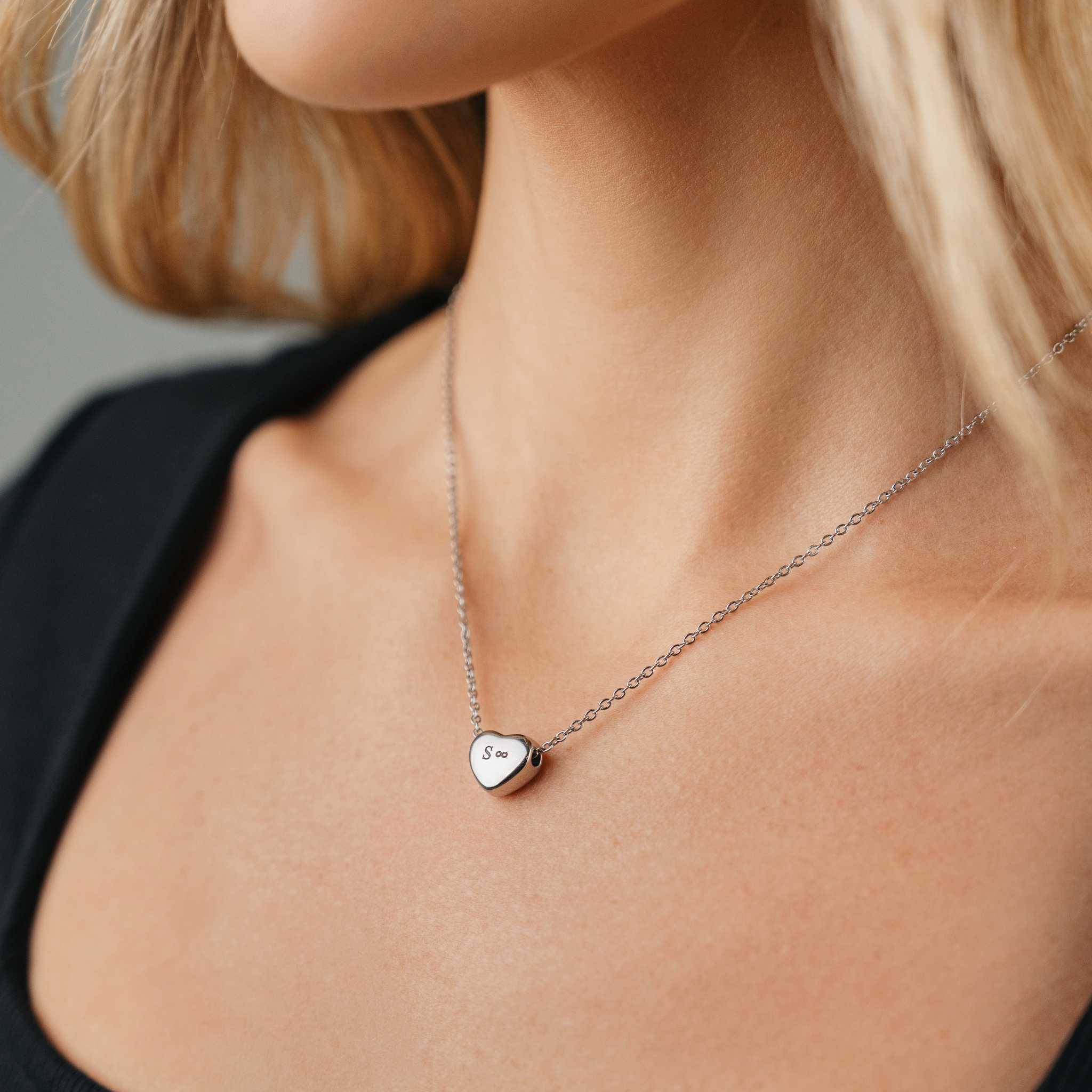 A female wearing SAAR CO's stainless steel heart pendant chain. The heart pendant is engraved with the letter S and the infinity symbol. 